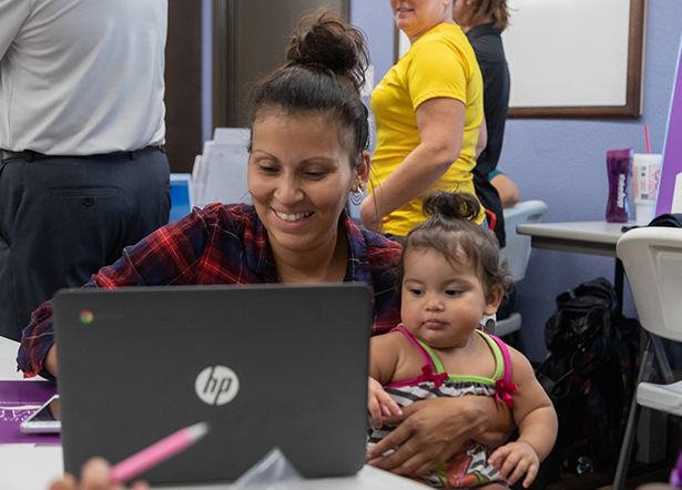 Photo of woman holding infant while working on laptop.